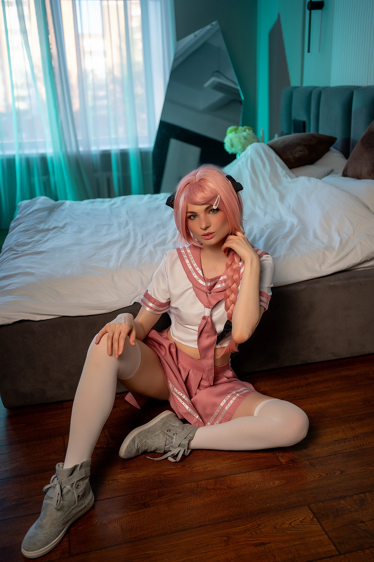 Astolfo femboy cosplay seated on floor with open legs in pink school uniform and white thigh-high socks under teal lighting