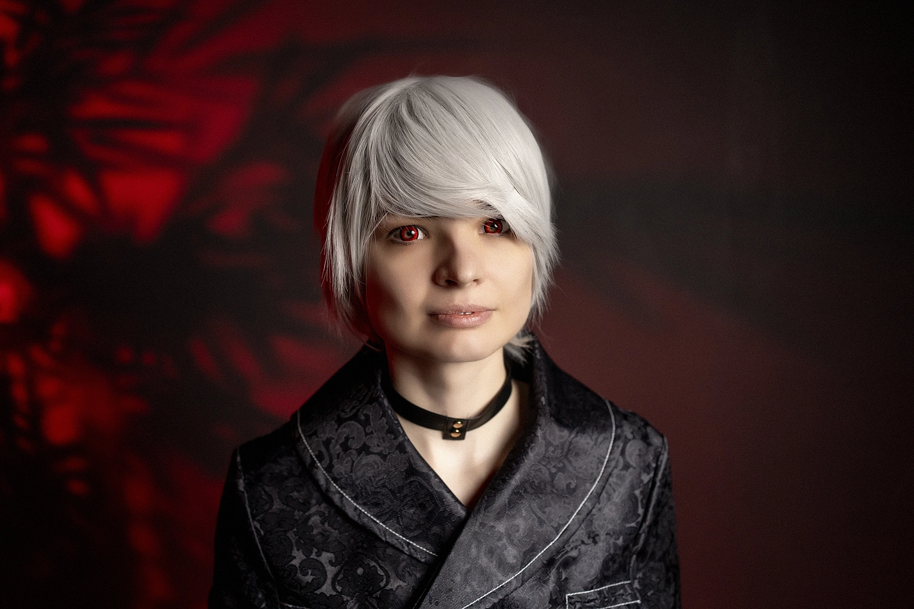 Cinematic 9S cosplay close-up with silver hair and dark YoRHa coat, warm red glow background.