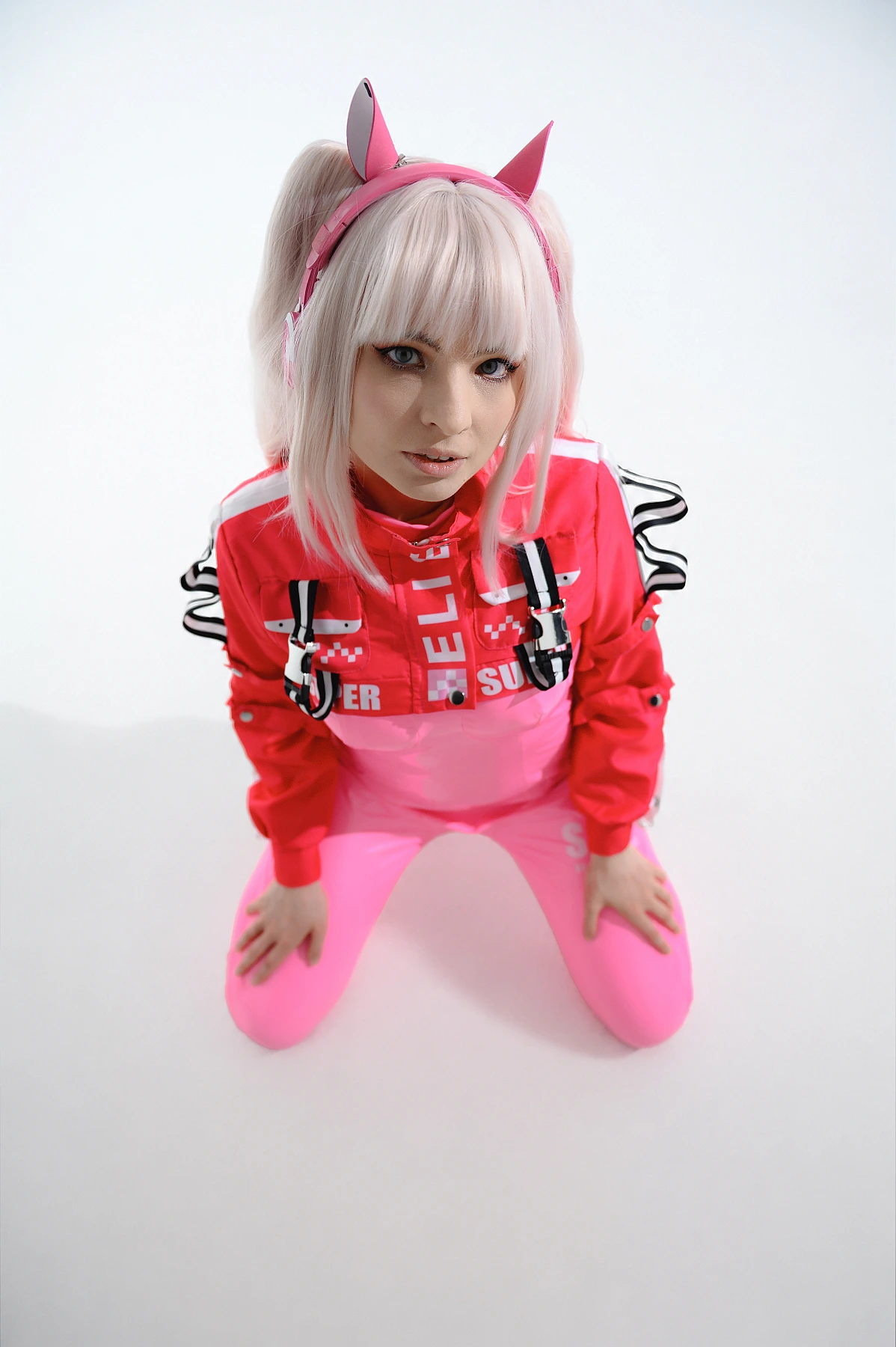 Top-down portrait of Alice cosplay from Goddess of Victory Nikke kneeling in a pink tactical outfit and looking at the camera