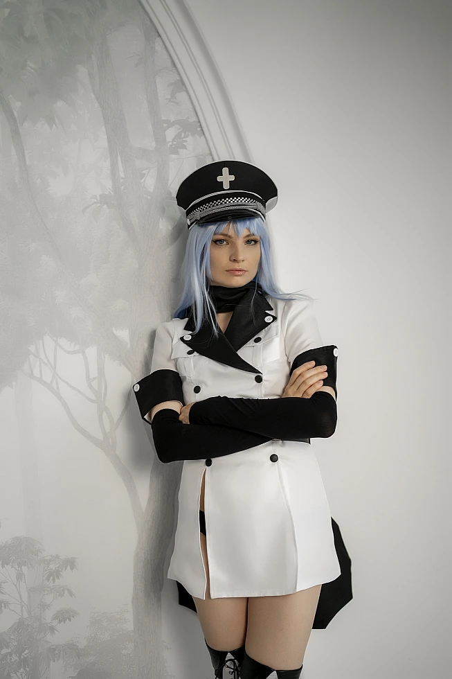 Esdeath cosplay from Akame ga Kill! leaning against a wall with arms folded, in white uniform and black peaked cap