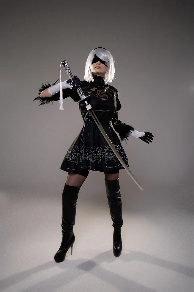 2B YoRHa cosplay frontal pose with katana extended forward, silver hair, black blindfold, NieR Automata costume in studio