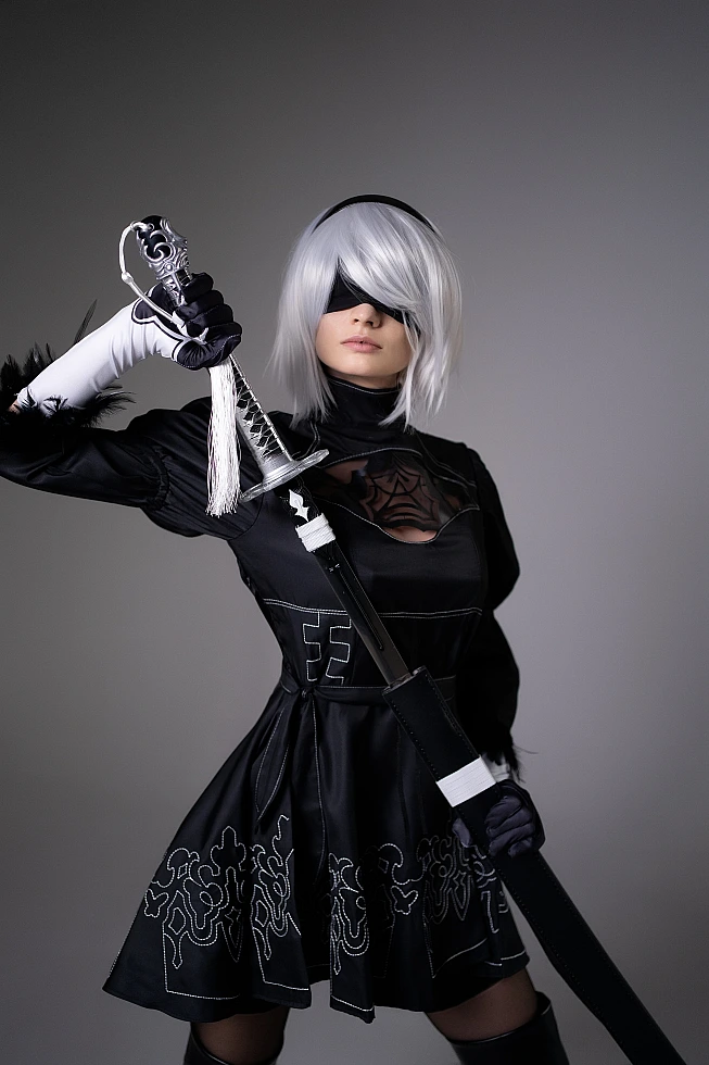 Close-up 2B NieR Automata cosplay portrait with blindfold and katana detail, silver bob wig, embroidered black dress
