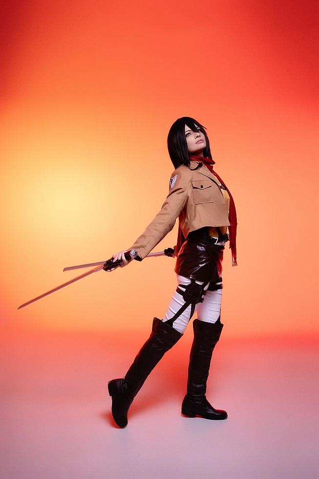 mikasa ackerman cosplay side profile with lowered dual blades and red scarf drape against warm orange backdrop