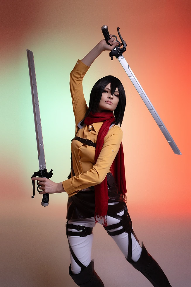 mikasa ackerman cosplay heroic pose with sword raised overhead and red scarf against warm gradient studio background