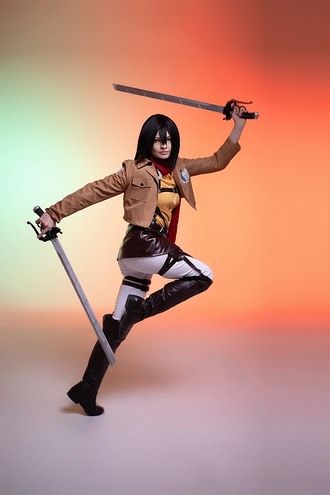 mikasa ackerman cosplay mid-air leap with dual blades extended and red scarf trailing against warm studio gradient