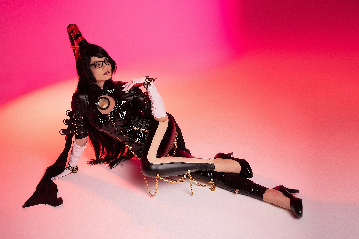 Bayonetta cosplay elegant side recline by Neka-Chi, glossy black bodysuit, gold chains, soft pink gradient background