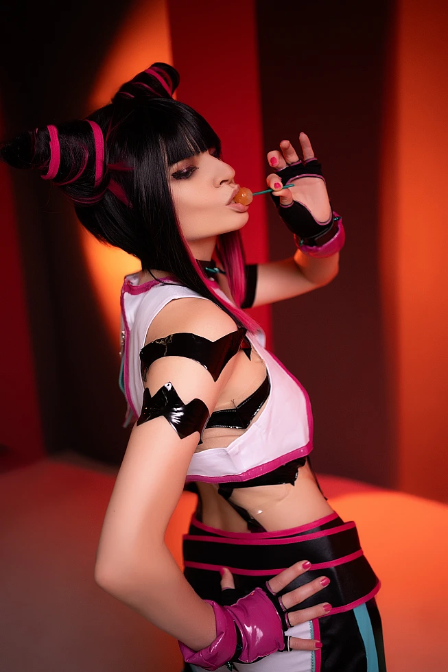 Juri Han cosplay side profile, candy at lips, hand on waist, warm orange-red neon background, glossy strap costume, horn buns