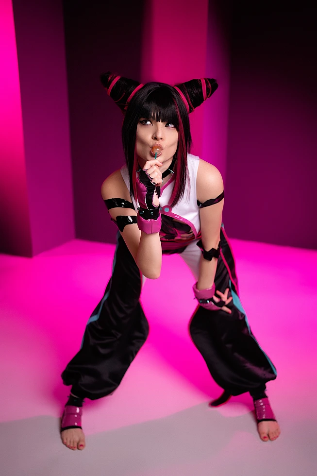 Juri Han cosplayer leaning forward with lollipop at lips, barefoot wide stance, neon pink studio lighting, glossy strap costume, Street Fighter