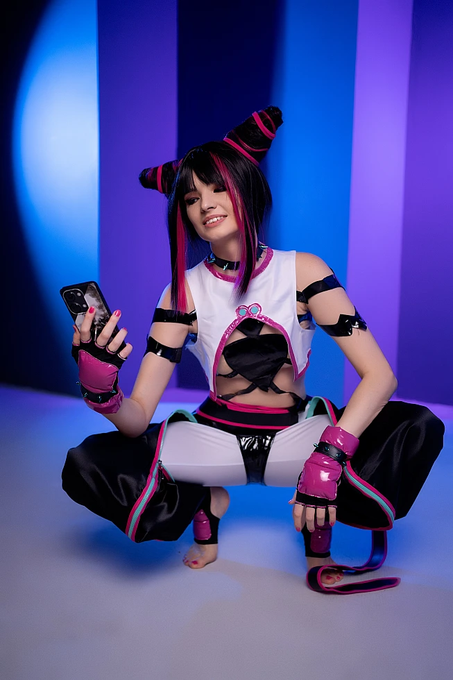 Juri Han cosplayer squatting with smartphone, cool blue-violet neon studio background, relaxed posture, glossy strap costume, Street Fighter