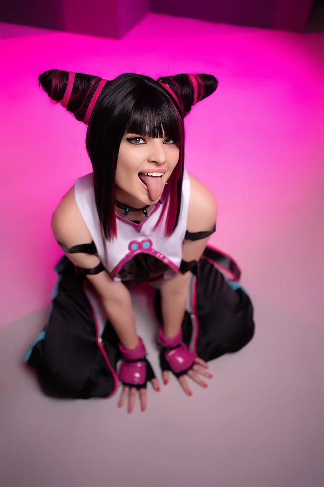 Juri Han cosplayer kneeling with tongue out, pink gradient lighting, white top with black straps, pink gloves, Street Fighter