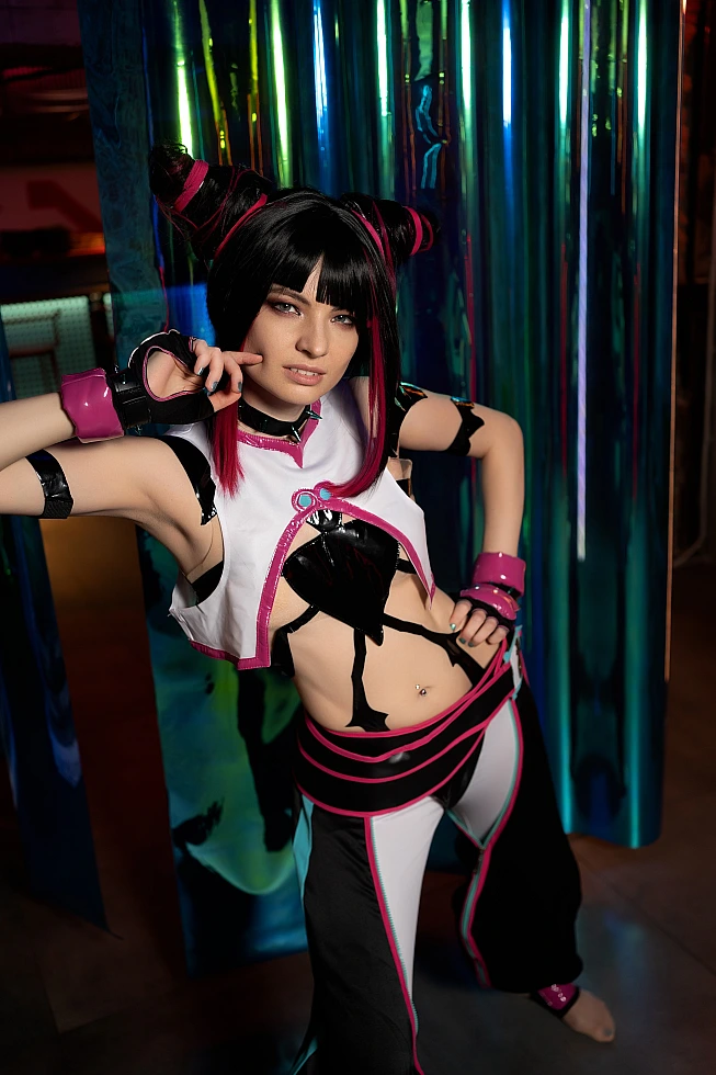 Juri Han cosplay near iridescent reflective panels with blue-green-gold gradients, direct gaze and glossy costume echoing colors