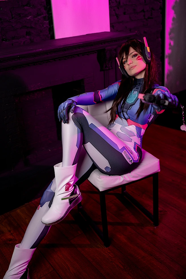 D.Va cosplay seated chair pose with extended leg, magenta neon lighting, futuristic Overwatch bodysuit, professional gaming cosplay