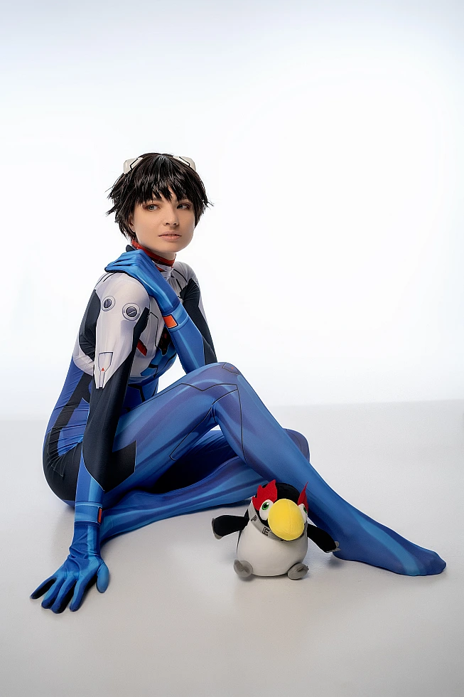 Shinji Ikari cosplay floor scene with plush toy, blue catsuit, extended legs, white studio backdrop, anime cosplay