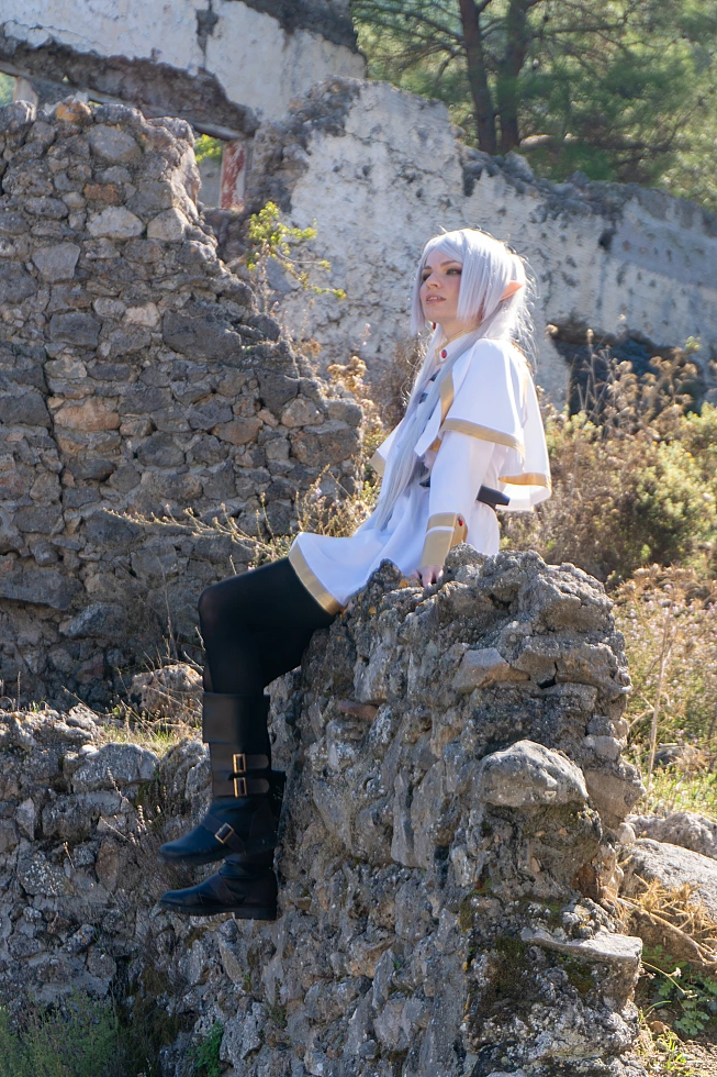 Frieren cosplay seated side profile stone ruins silver hair elf ears white gold dress dry grass soft daylight Sousou no Frieren