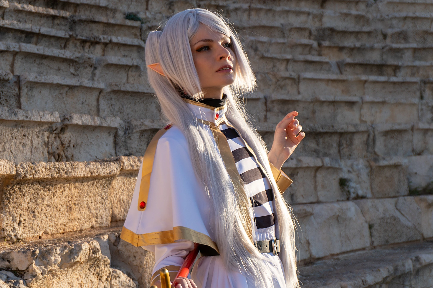 Frieren cosplay warm sunlight profile portrait silver hair elf ears white gold outfit textured stone wall natural light