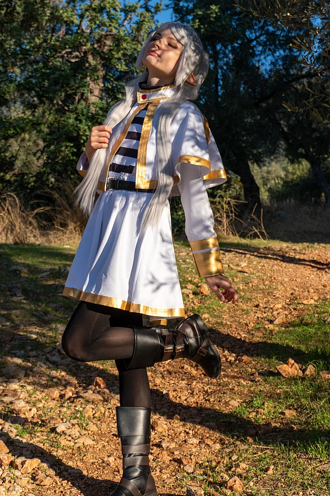 Frieren cosplay standing one leg forest clearing silver hair elf ears white gold mage dress dappled sunlight calm pose