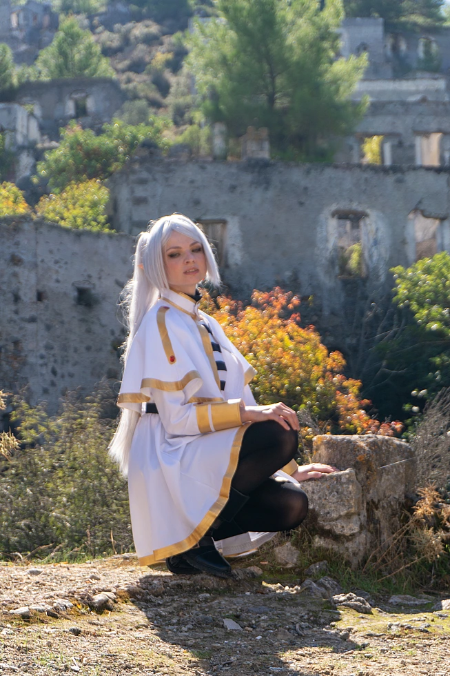 Frieren cosplay crouching weathered stone silver hair elf ears white gold mage costume autumn foliage ancient ruins daylight