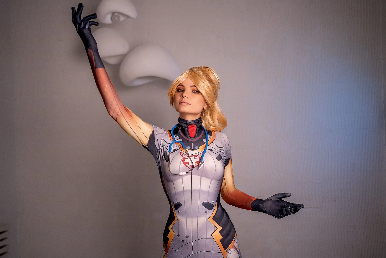 Mercy Overwatch cosplay standing pose with raised open-arm gesture, detailed medical bodysuit, minimal white studio background