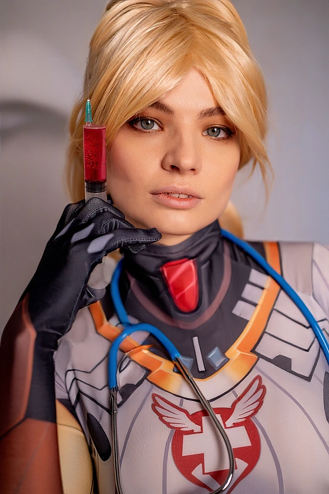 Mercy Overwatch cosplay close-up face portrait with syringe prop, detailed makeup, suit emblem visible, soft lighting
