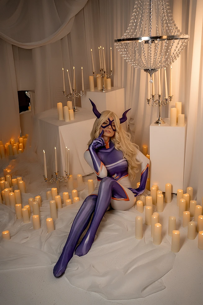 Mt. Lady cosplay seated pose with extended legs, horned mask and glossy catsuit in candlelit studio