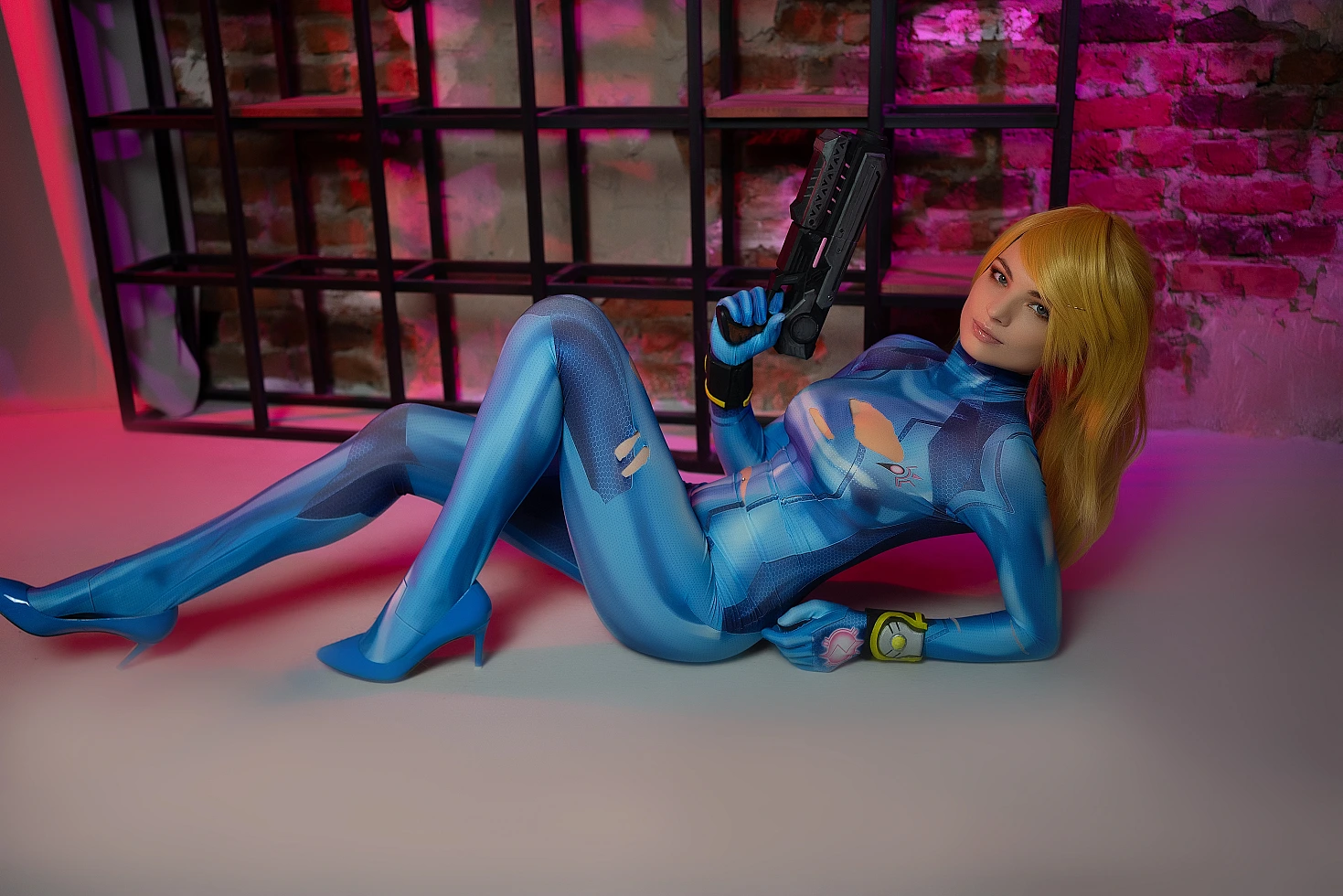 Zero Suit Samus cosplay reclining pose, blaster prop, glossy blue bodysuit, neon pink magenta lighting, industrial studio