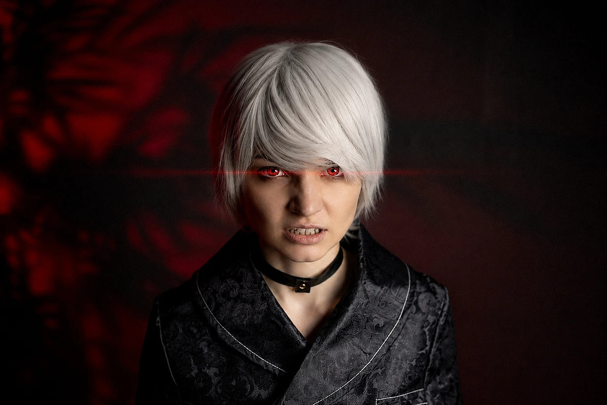 Cinematic 9S cosplay close-up with silver hair and dark YoRHa coat, warm red glow background.