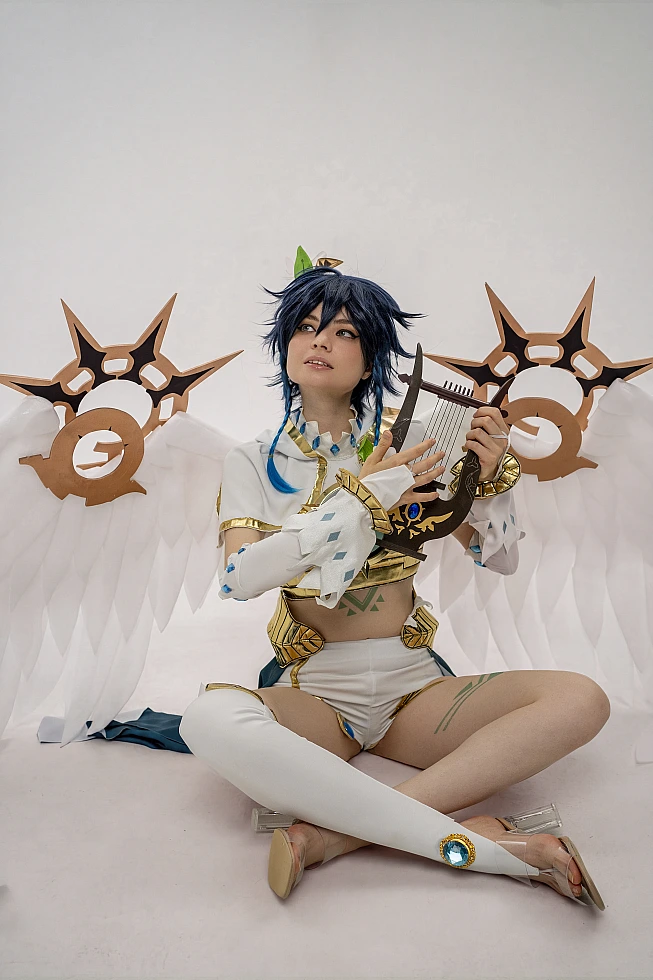 Venti cosplay from Genshin Impact sits on the floor holding an ornate lyre, white wings spread behind.