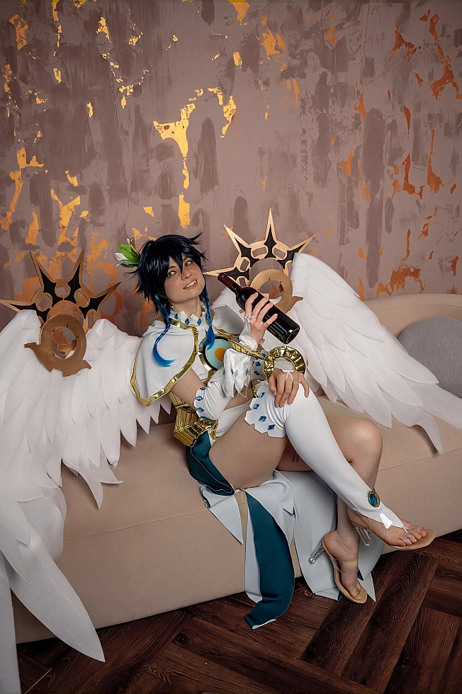 Venti cosplay from Genshin Impact lounges on a beige sofa with large white angel wings spread behind.