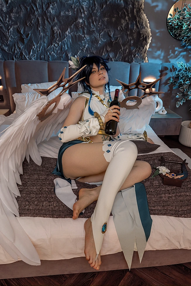 Venti cosplay from Genshin Impact sits on a bed holding a wine bottle, with large white wings behind.