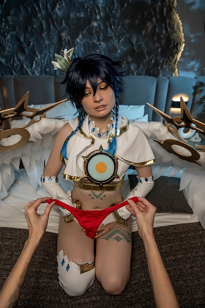 Venti cosplay from Genshin Impact kneels on a bed with white wings while red lingerie hangs in front.