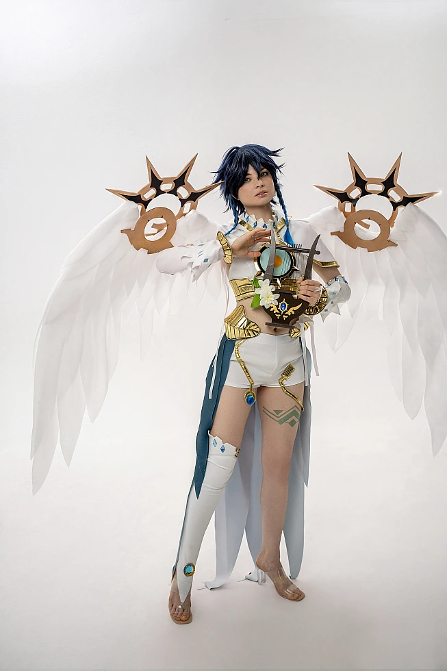 Venti cosplay from Genshin Impact stands full-body in a studio holding a small lyre, white wings spread wide.