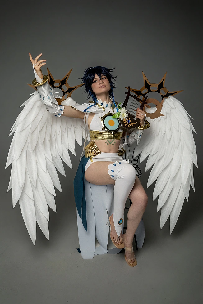 Venti cosplay from Genshin Impact sits holding a lyre with one arm lifted, white feathered wings spread behind.