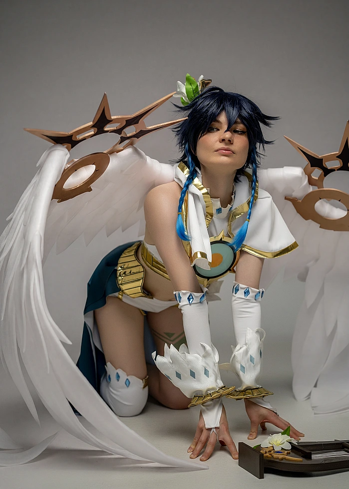Venti cosplay from Genshin Impact kneels forward between large white wings, reaching toward a lyre on the floor.
