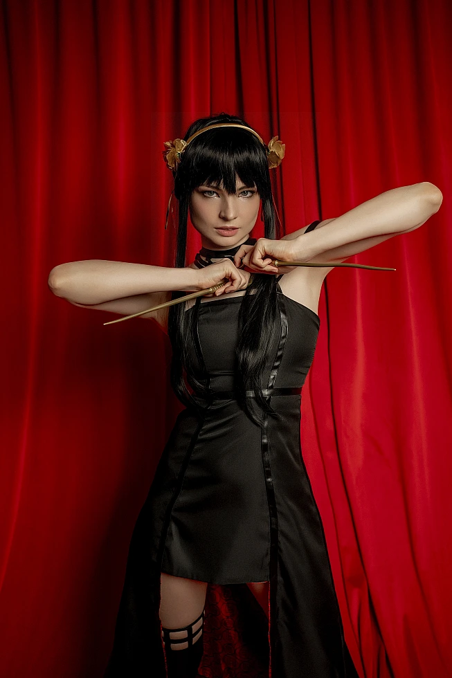 Yor Forger from Spy x Family faces the camera in front of a red curtain, elbows high, drawing two gold stilettos apart.