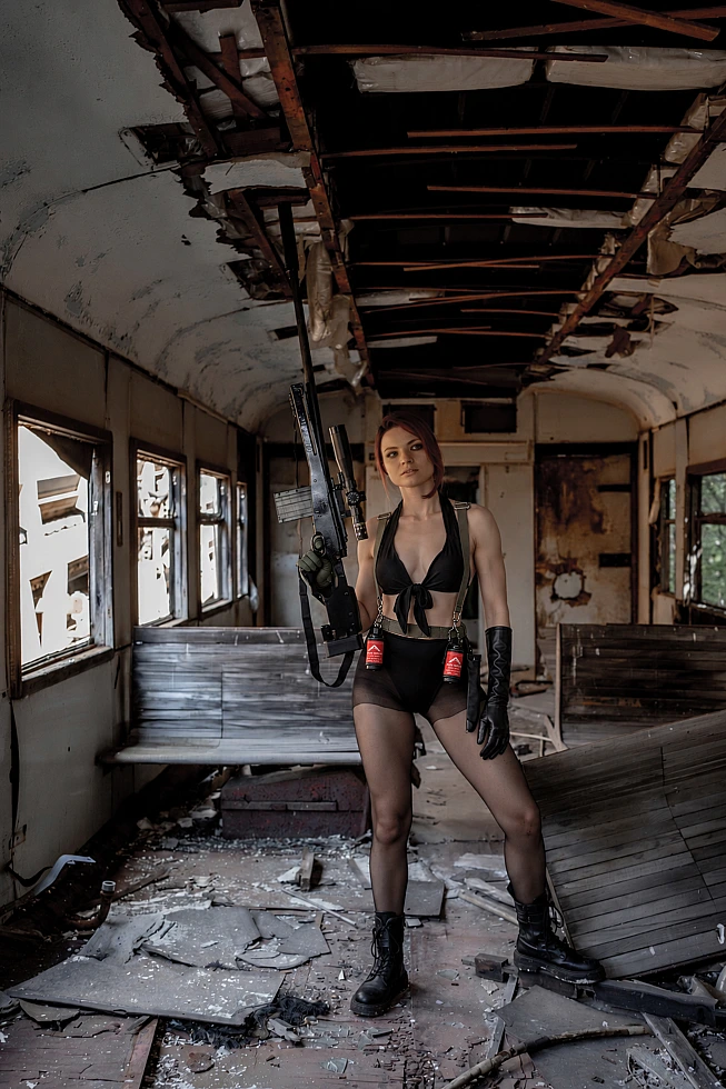 Quiet cosplay standing inside a wrecked abandoned passenger carriage with a collapsed ceiling and a sniper rifle